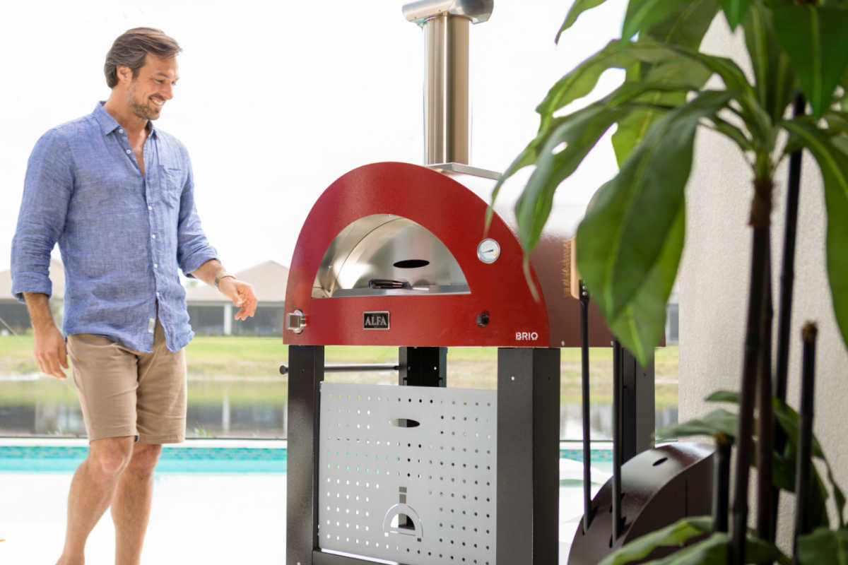 Large Pizza Oven on a stand in an outdoor entertaining area with a man looking at it.