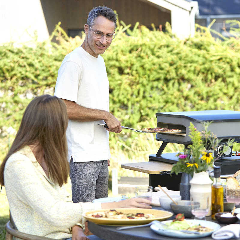Man cooking a pizza with the Cozze pizza oven in a family setting.