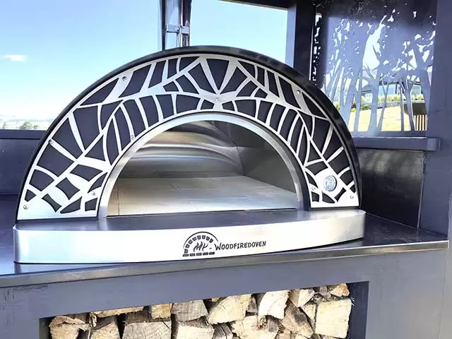 Medium sized pizza oven on a bench with wood stacked underneath. 
